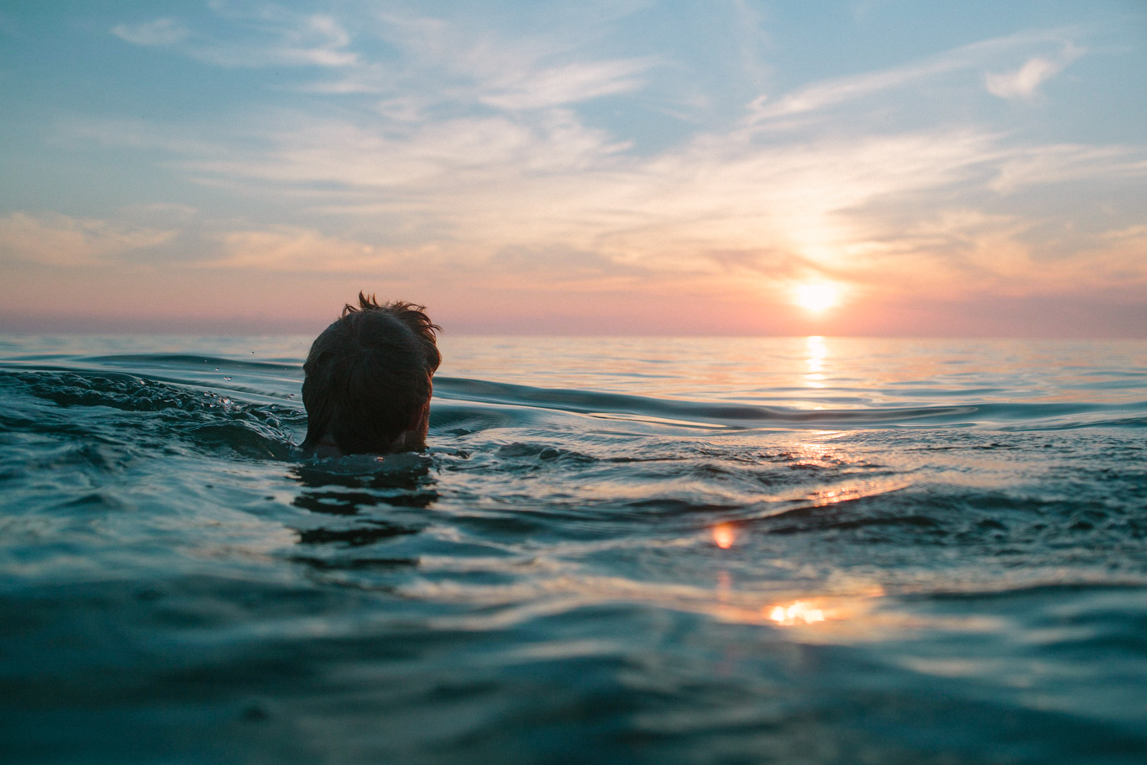 A person's head sticking out of a body of water looking at the sunset.